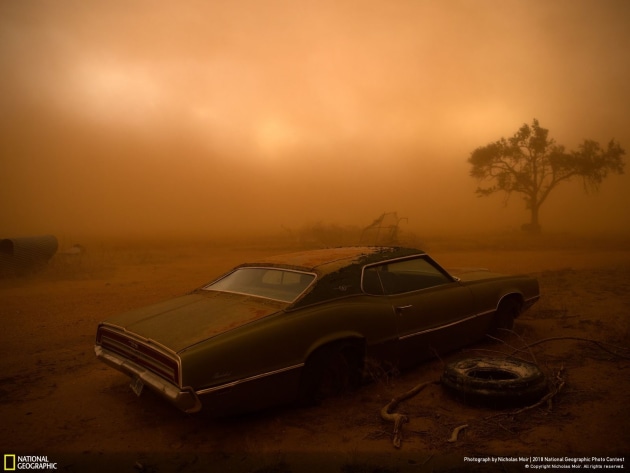 Photograph and caption by Nicholas Moir / 2018 National Geographic Photo Contest. A rusting Ford Thunderbird is blanketed by red dust from a supercell thunderstorm in Ralls, Texas. The dry, plowed fields of the Texas Panhandle made easy prey for the storm, which had winds over 90 miles an hour ripping up the topsoil and depositing it farther south. I was forecasting and positioning a team of videographers and photographers on a storm chase in Tornado Alley—this was our last day of a very successful chase, having witnessed 16 tornadoes over 10 days. The target area for a storm initiation was just south of Amarillo, Texas. Once the storm became a supercell, it moved southbound with outflow winds that were easily strong enough to tear up the topsoil and send it into the air.