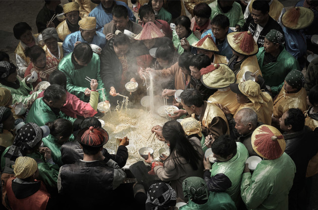 © Jianhui Liao, China. WINNER - FOOD (SINGLE IMAGE CATEGORY). Shanxi, China. A crowd gathers to eat from a huge dish of noodles.