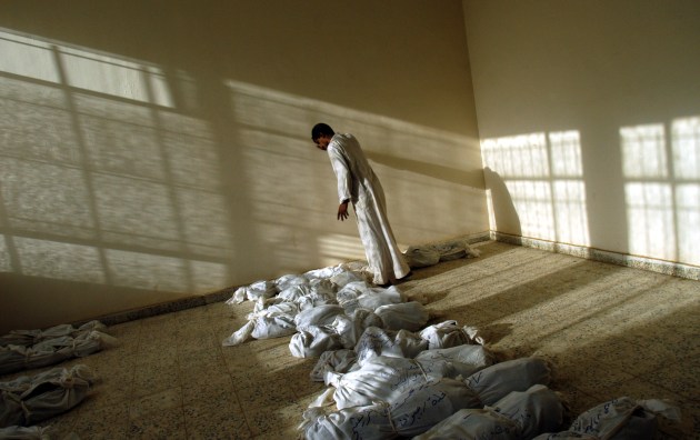 An Iraqi man leans against the wall as he walks along rows of remains of bodies discovered in a mass grave south of Bagdad, and laid out in a building in Iraq, 29 May, 2003. © Lynsey Addario.