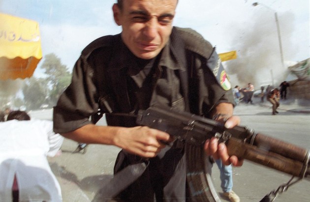 © Ami Vitale. A Palestinian soldier runs from a police station as it is bombed by an Israeli helicopter in the West Bank town of Ramallah, 12 October, 2000.