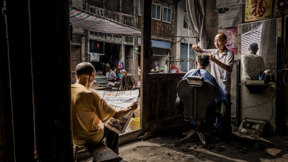 Window
Photographer: Huamin Luo

"It was taken in my hometown, PanShi town, Dazhou, Sichuan Province, China on July 19, 2018. People still maintain living the traditional lifestyle there, in the old barbershop, while a barber is busy taking care of an old customer's hair, through the window the customers are watching other residents rushing to the market. People waiting in lines are leaning on the door, and reading newspapers. The life on the street is quiet, and this all reminds me of my childhood."