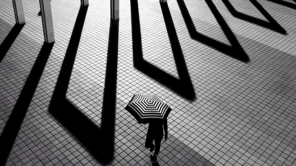A finalist in the Mobile category – a woman carrying a striped black and white umbrella passes some gates (Credit: Laurence Bouchard)