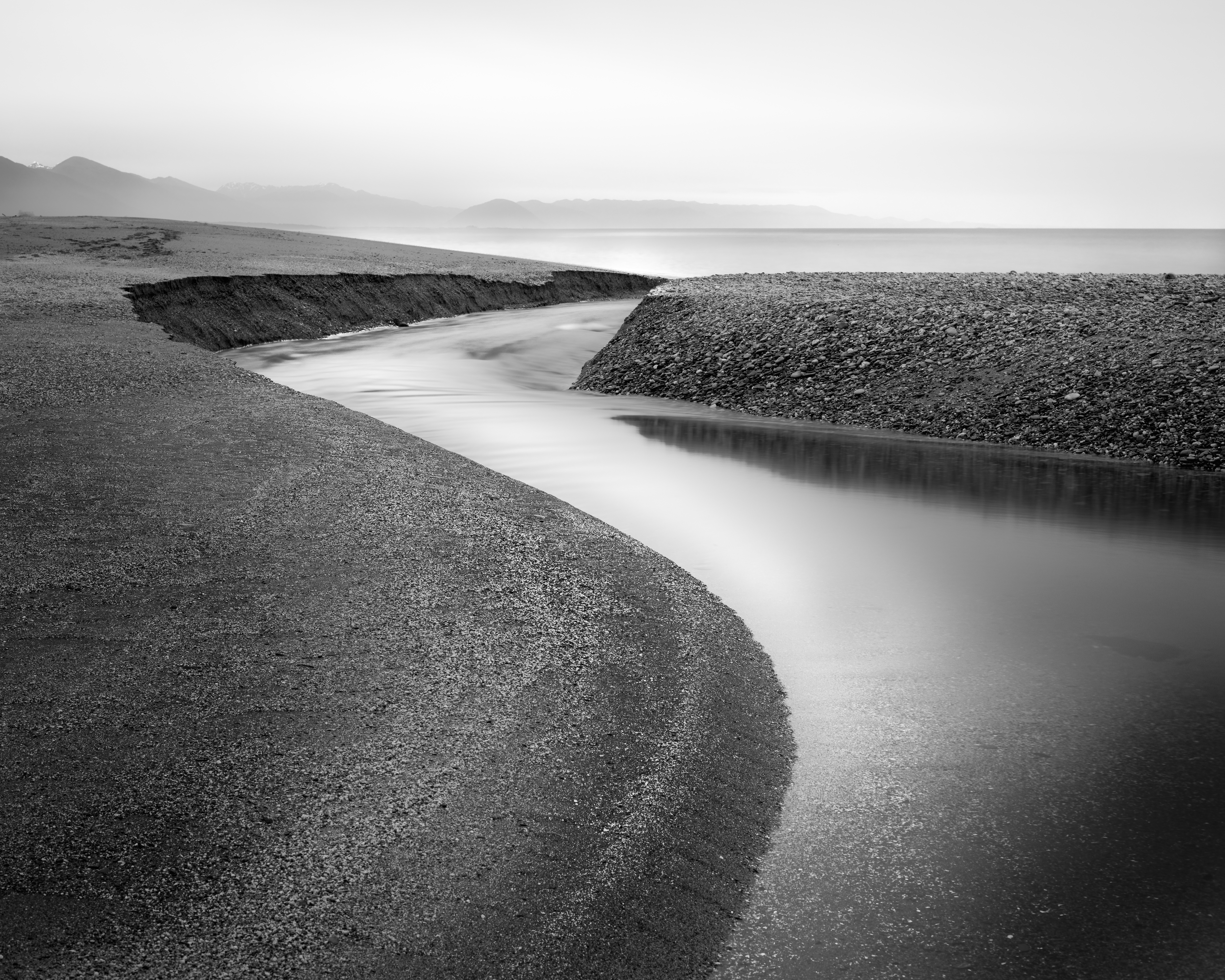 West Coast, New Zealand. Converting to black and white simplifies this already minimal landscape further, enhancing the beautiful curve and flow of the stream as it winds toward the sea. Nikon D850, Nikkor 50mm f1.8 lens @ 50mm. 30s @ f11, ISO 64.