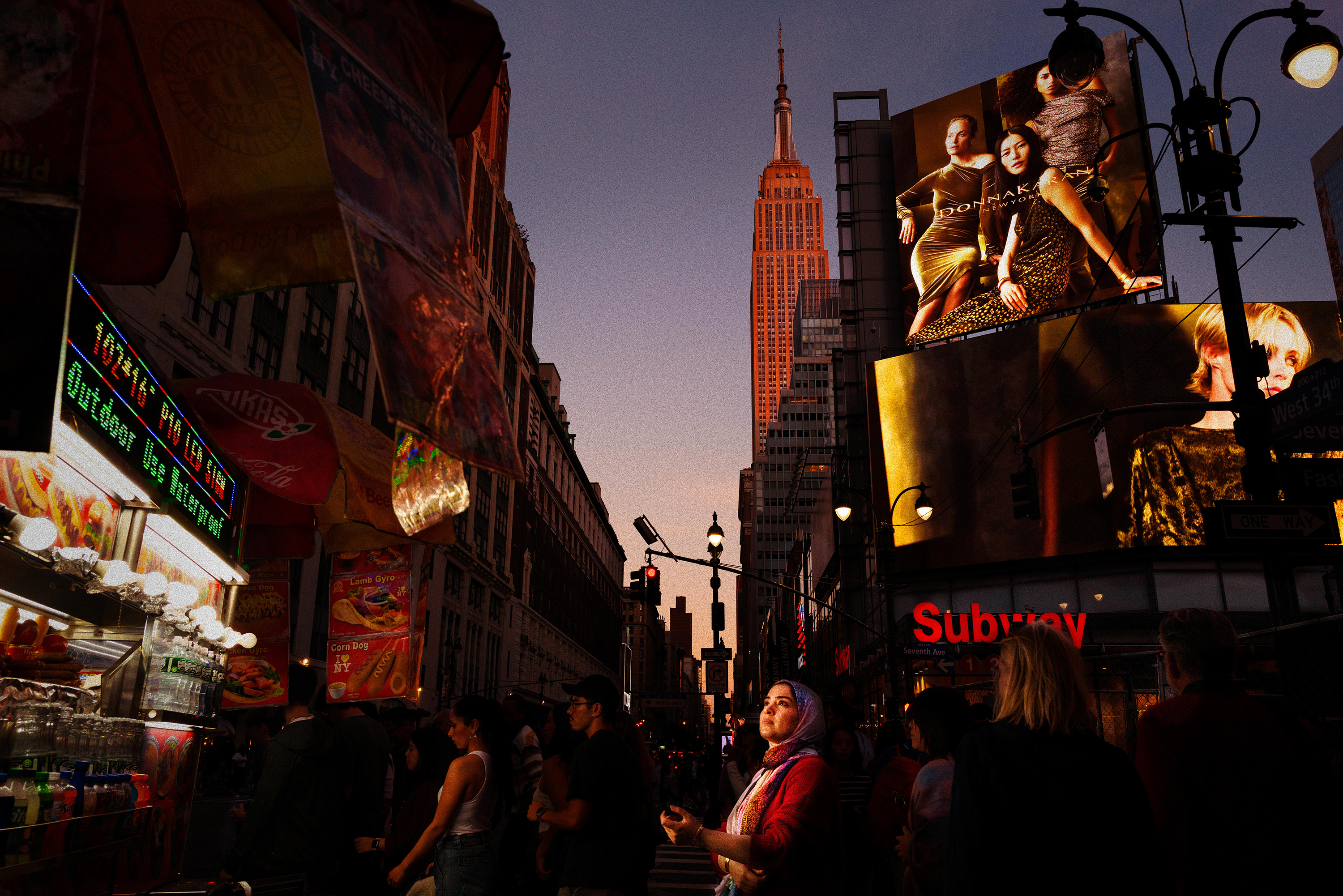 Empire State Building, MidtownAs the evening sun ignites the Empire State Building, Midtown glows in neon from colossal billboards, while the halogen glare of food carts casts passersby in spotlight — as if on a film set.