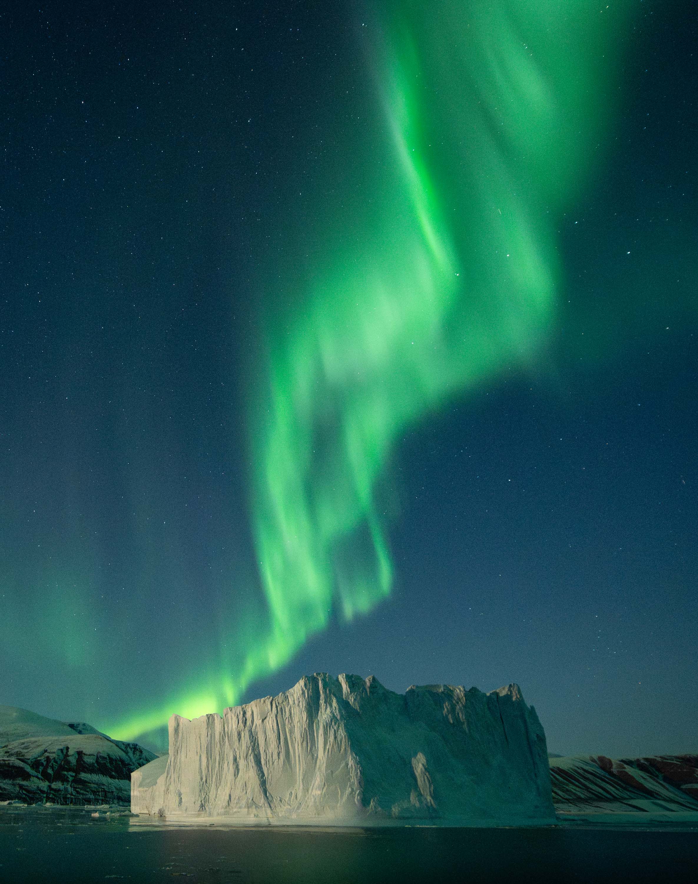 “Twisting Turn” – Virgil ReglioniScoresbysund, GreenlandBehind every image lies a deliberate process — a fusion of coordination, timing, and technical precision carried out from a ship navigating some of the harshest conditions on Earth. Photographing the aurora over the ice is never about luck; it’s the result of preparation, teamwork, and experience. From the ship’s bridge to the camera deck, every movement is carefully planned to give the lights their best possible stage.During the day, we navigated through fields of icebergs, scouting for the perfect one — a curve, a ridge, or a translucent arch to anchor the composition. Guided by how the aurora moves across the Greenlandic sky, we aligned our chosen iceberg and ship precisely, uniting earth, ice, and sky in one luminous image.