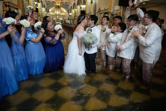 Title: Wedding in the Flood. © Aaron Favila, Associated Press.
Newlyweds share a kiss as guests cheer. The couple have been together for ten years. According to Verdillo, “This is just one of the struggles that we’ve overcome.” Malolos, Bulacan province, Philippines, 22 July 2025.